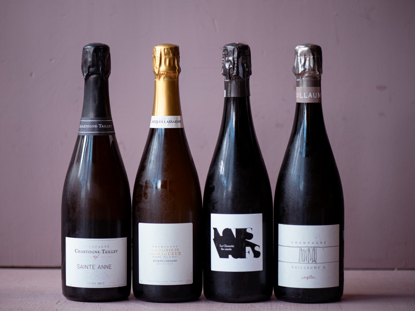 Four Champagne bottles lined up against a muted pink background.