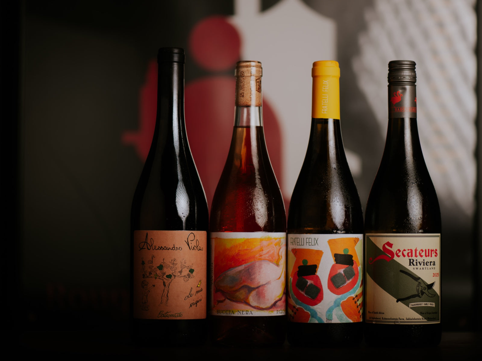 Four bottles of skin-contact wine against a graphic black, white and red backdrop.