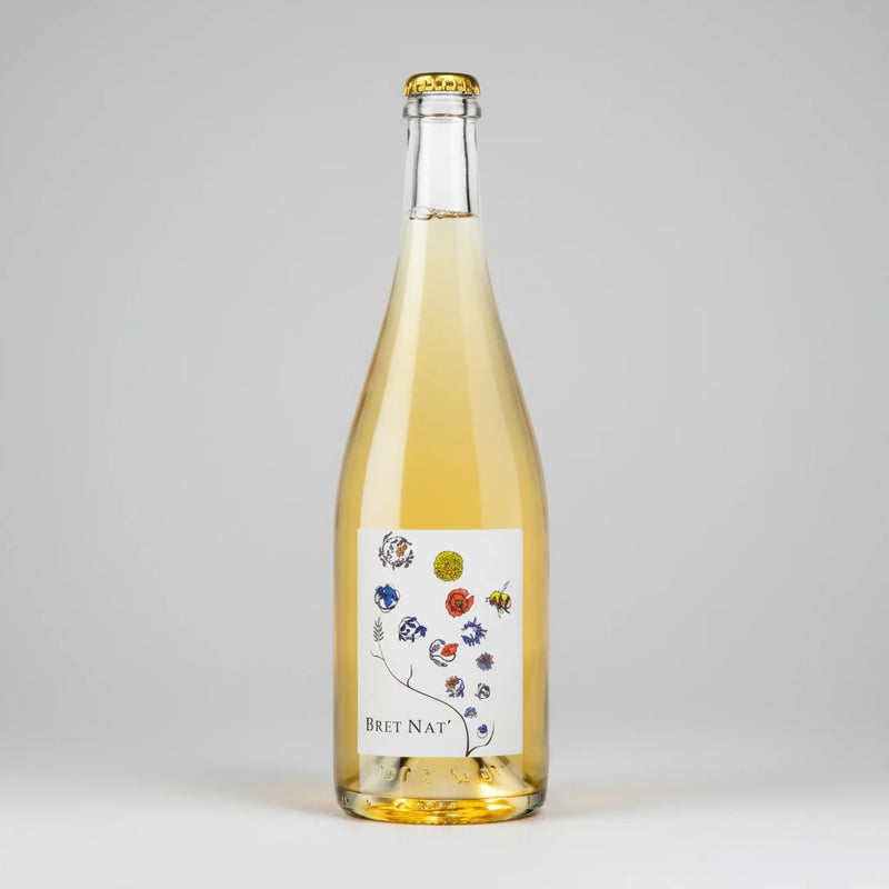 A bottle of Bret Brothers Bret Nat with pale golden liquid, featuring a white label with colorful botanical illustrations and a gold crown cap, set against a plain white background.