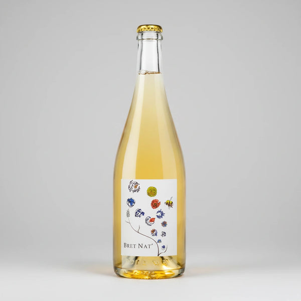 A bottle of Bret Brothers Bret Nat with pale golden liquid, featuring a white label with colorful botanical illustrations and a gold crown cap, set against a plain white background.