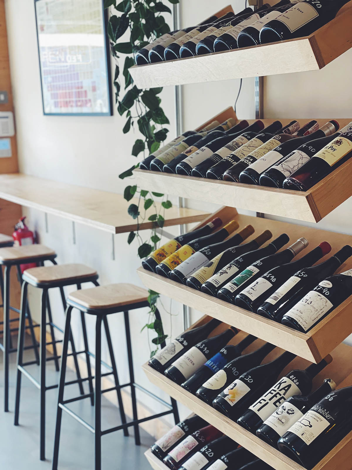 Wine bottles displayed on a wooden rack in a bar setting with stools and a counter.